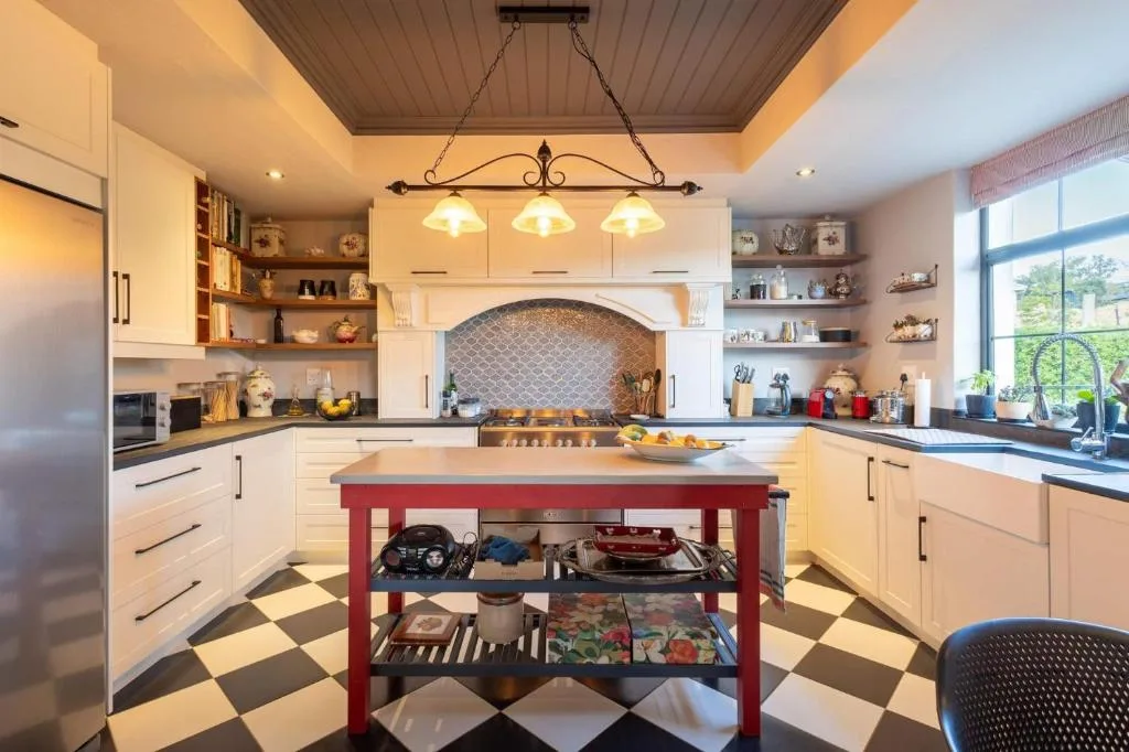 Modern kitchen with cream cabinetry, red island, pendant lighting, and open shelving