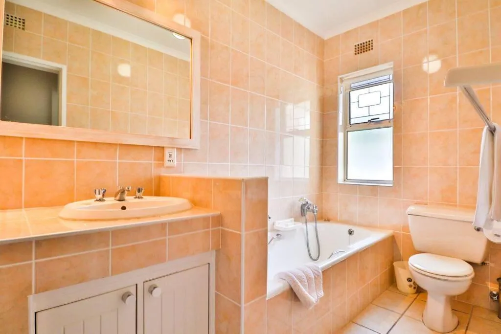 Spacious bathroom with peach tiles, vanity sink, bath tub, and toilet