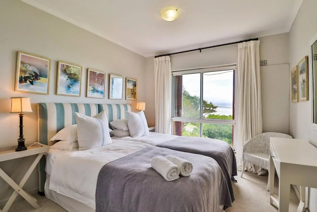 Bright bedroom with dual beds, striped headboard, ocean views through large windows