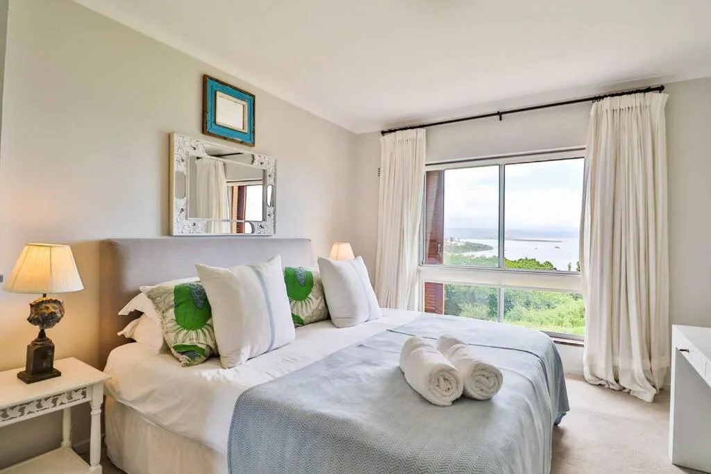 Bright bedroom with water view, queen bed, rolled towels, coastal decor