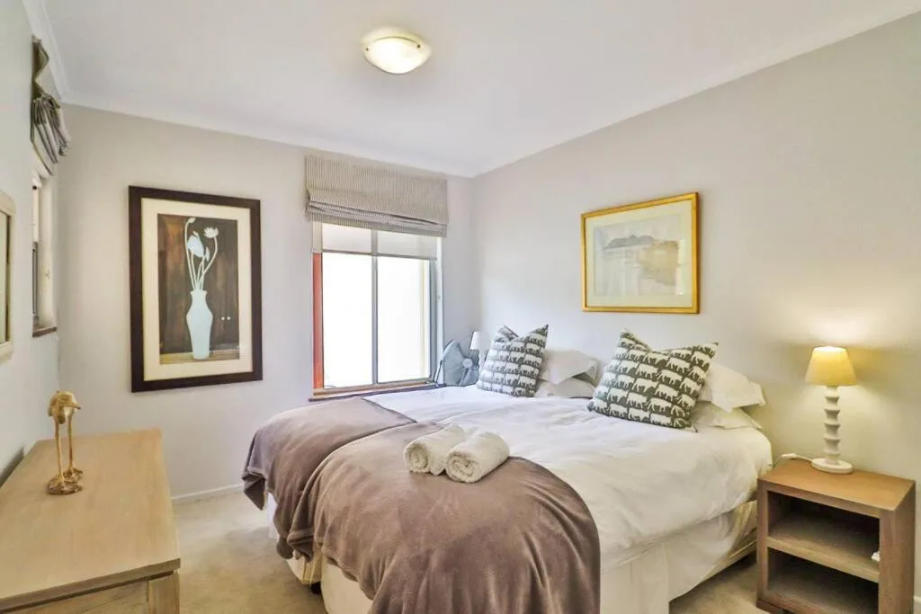 Bright bedroom with queen bed, patterned cushions, framed artwork, and sliding door access