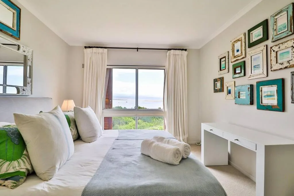 Bright bedroom with ocean view through large windows and coastal artwork