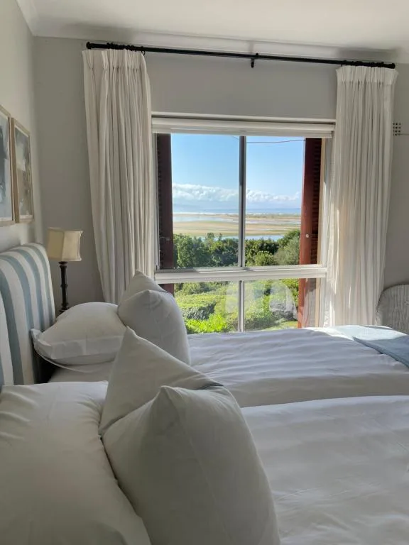 Bright bedroom with two beds and expansive window overlooking coastal landscape