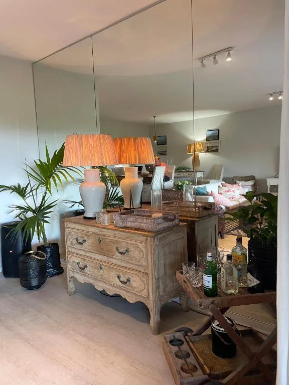 Bedroom vanity with wooden dresser, orange lamp, large mirror, potted plants
