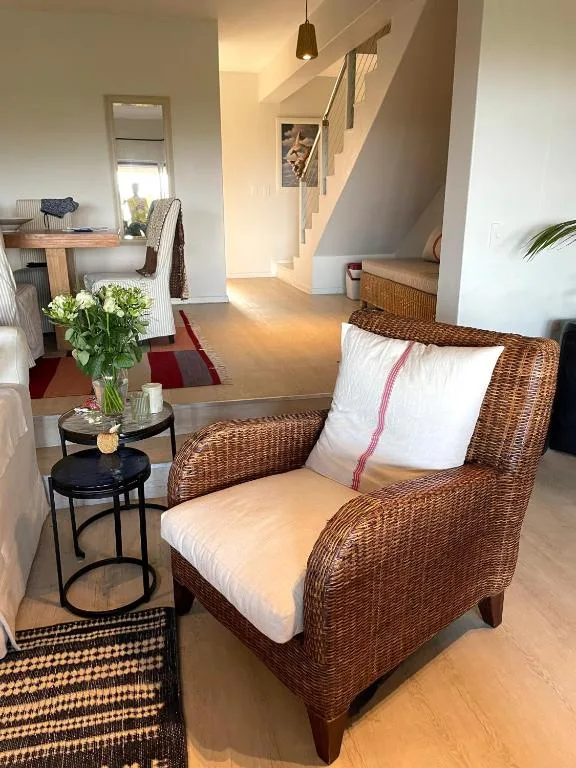 Bright living area with wicker armchair, side tables, and staircase beyond