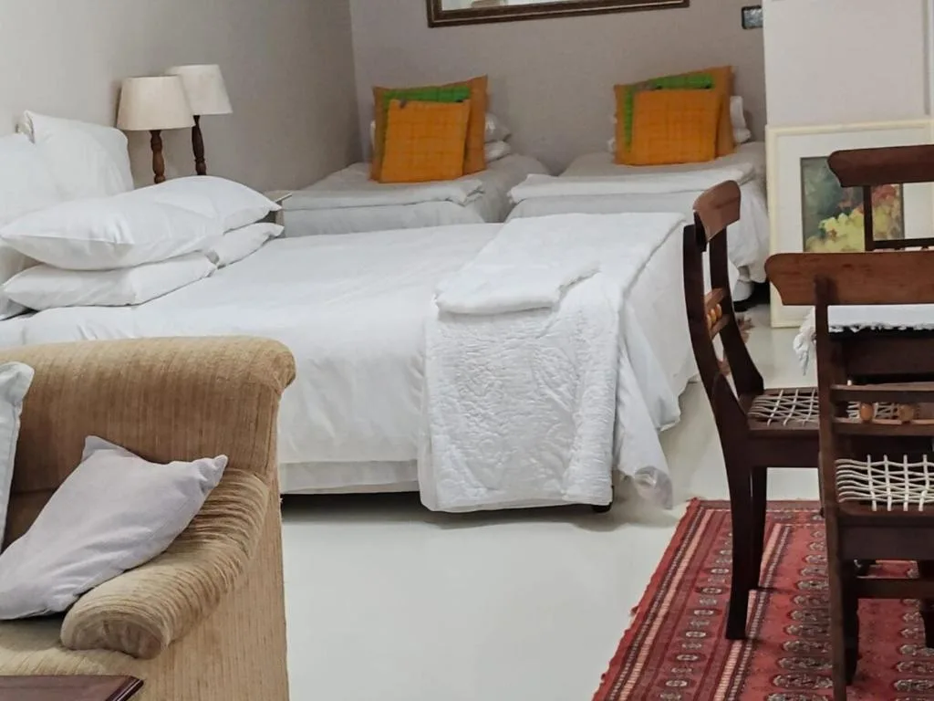 Spacious bedroom with multiple beds, white linens, and colorful orange pillows