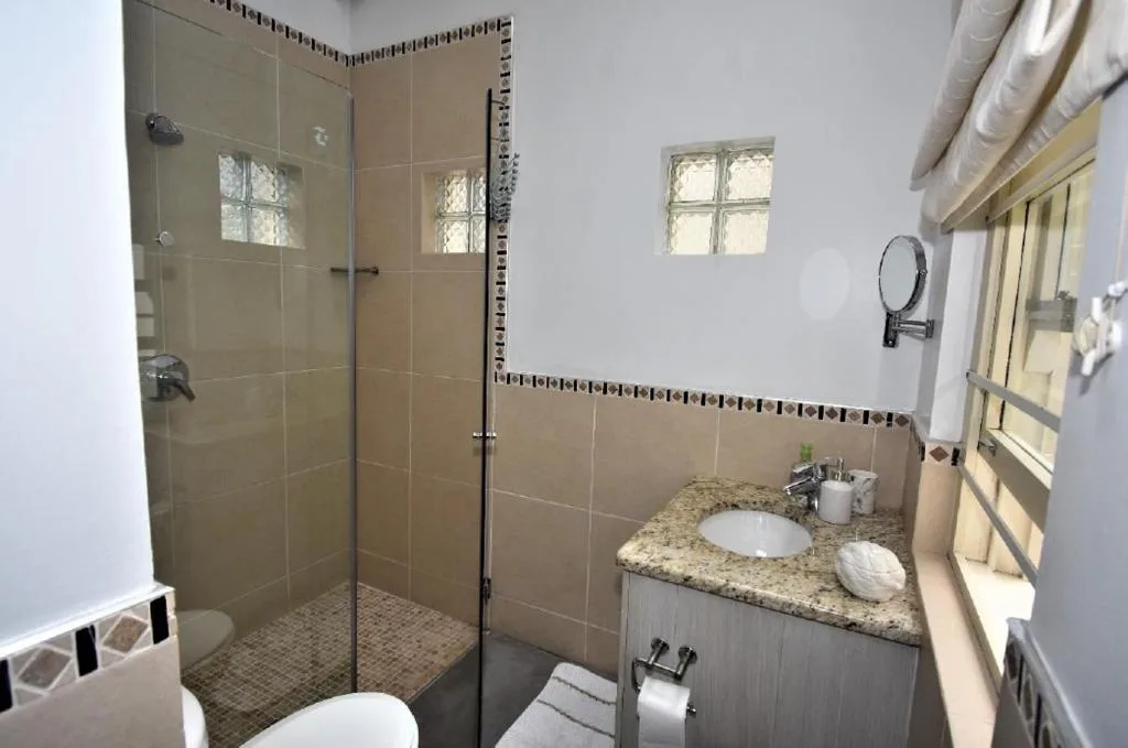 Modern bathroom with glass shower enclosure, granite vanity, and window
