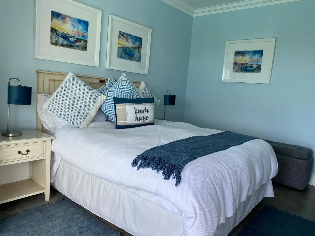 Coastal-themed bedroom with white bedding, blue pillows, and framed ocean artwork