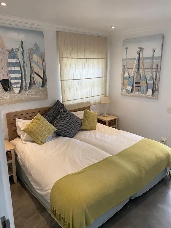 Bright bedroom with queen bed, yellow blanket, nautical wall art, and sheer curtains