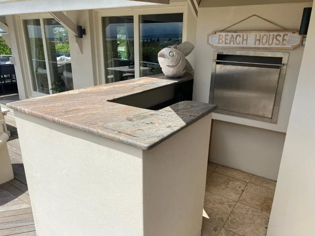 Outdoor kitchen counter with grill on covered patio area overlooking garden