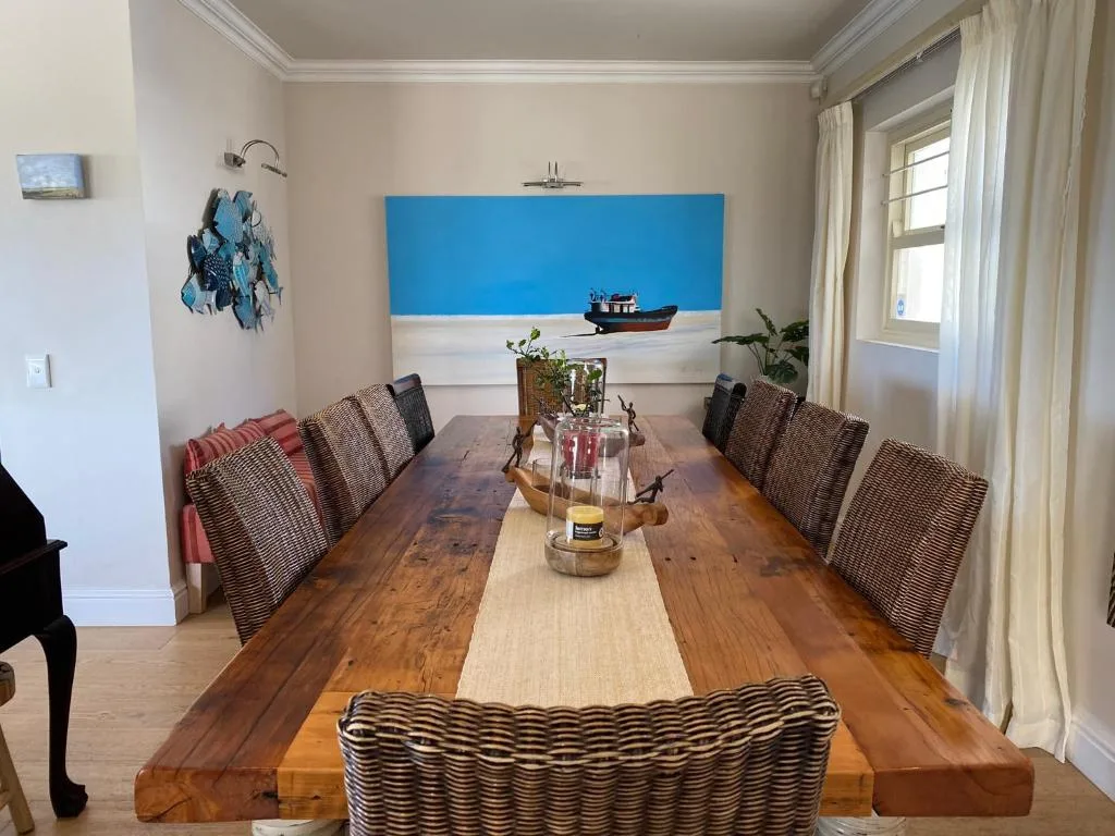 Wooden dining table with wicker chairs and coastal artwork on wall