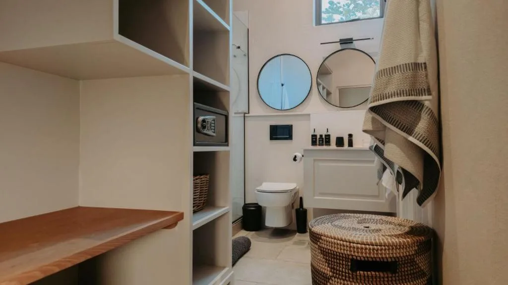 Modern bathroom with round mirrors, toilet, shelving, and woven storage baskets