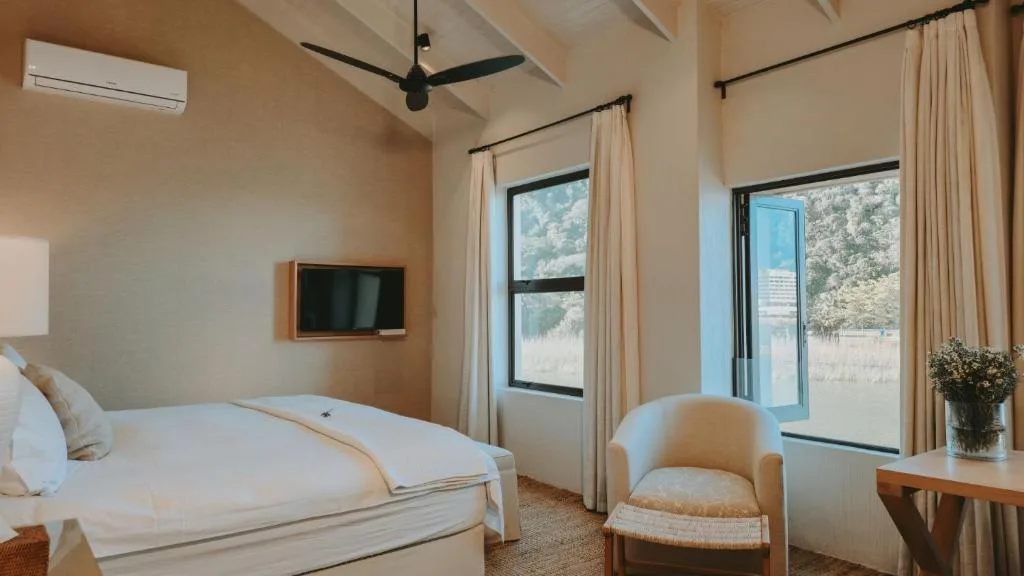 Bright bedroom with queen bed, mounted TV, and garden views through windows