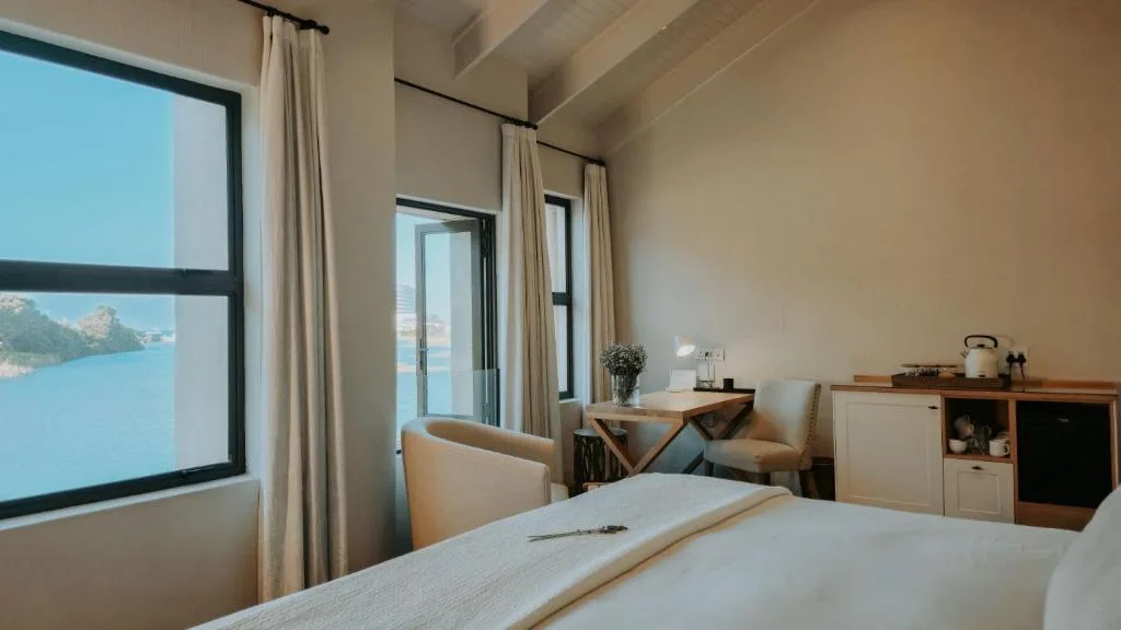 Bright bedroom with bed, desk, water views through large windows