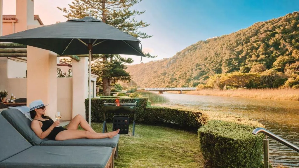 Woman relaxing on lounge chair under umbrella with river and mountain views