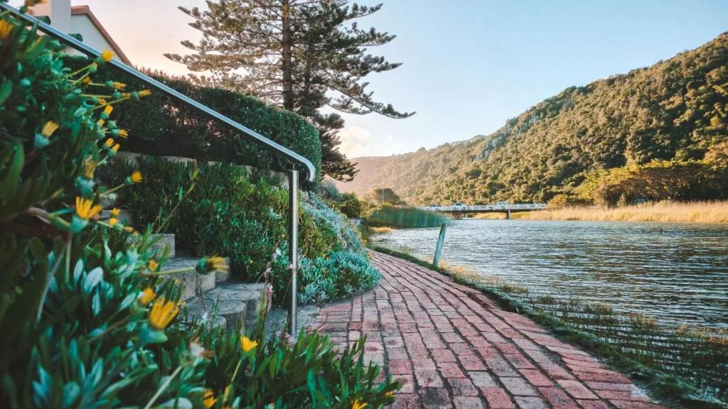 Wooden deck with flowering plants overlooking serene lagoon and forested hills