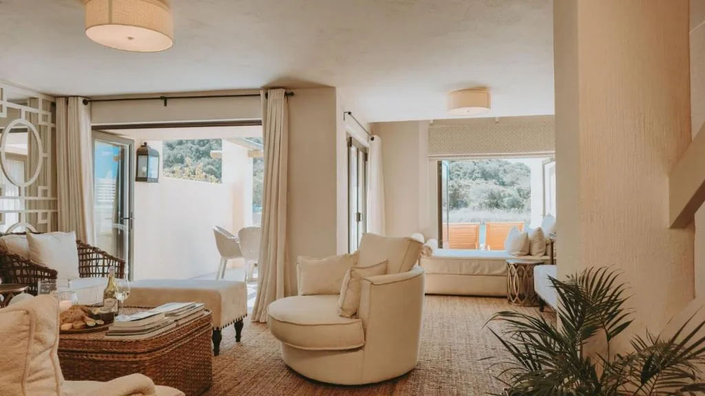 Bright lounge with cream armchairs, sofa, and scenic garden views through large windows