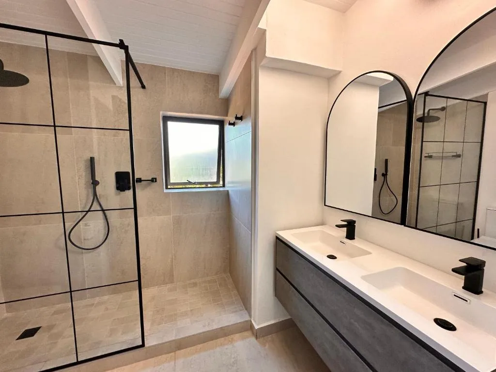 Modern bathroom with dual vanity, large mirror, and walk-in shower enclosure