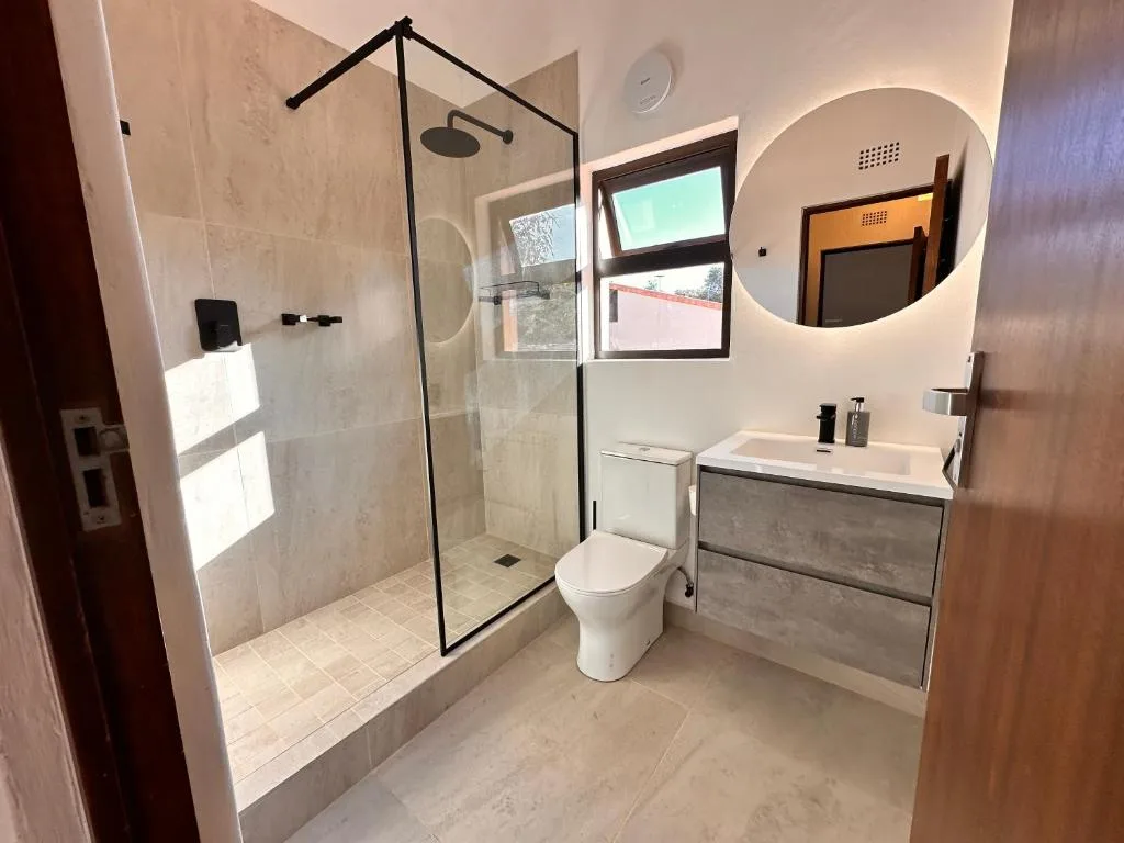 Modern bathroom with walk-in shower, toilet, vanity sink, and round mirror