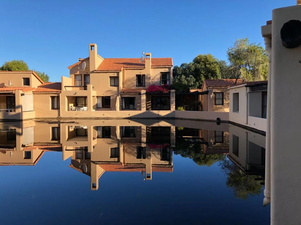Mediterranean-style apartment building reflected in still water under blue sky