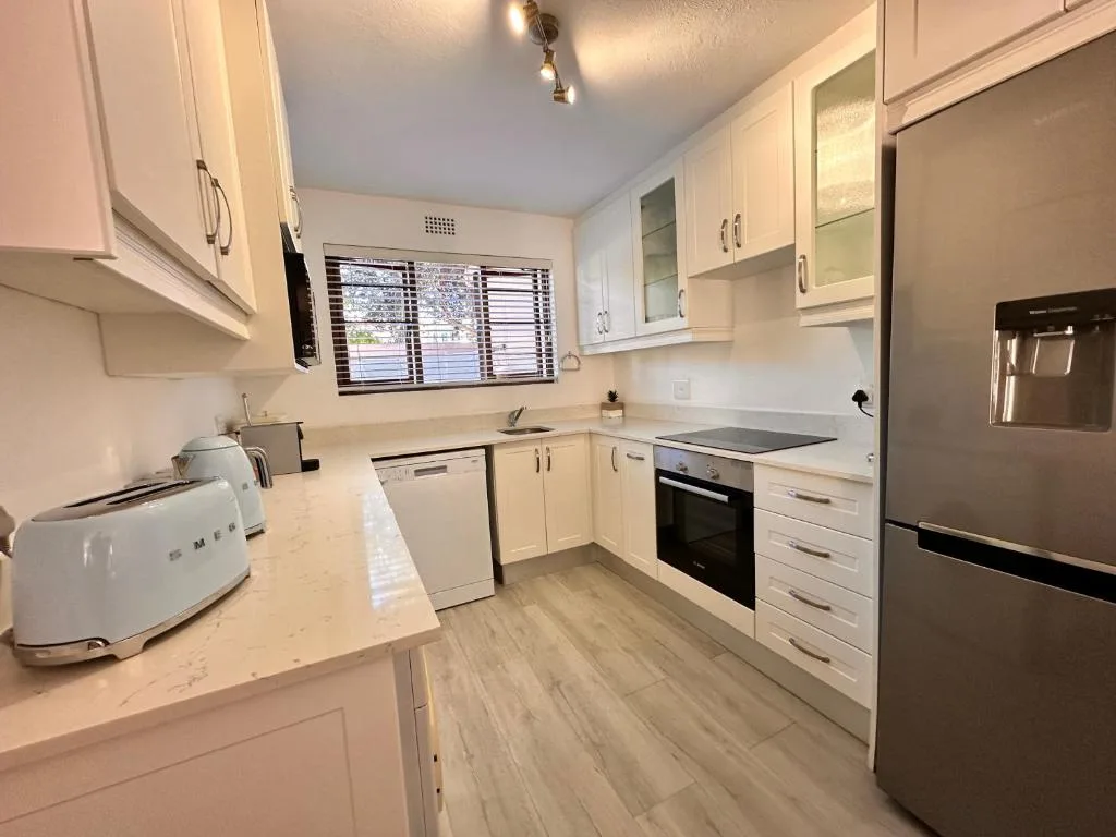 Modern kitchen with white cabinetry, stainless steel appliances, and wood-effect flooring