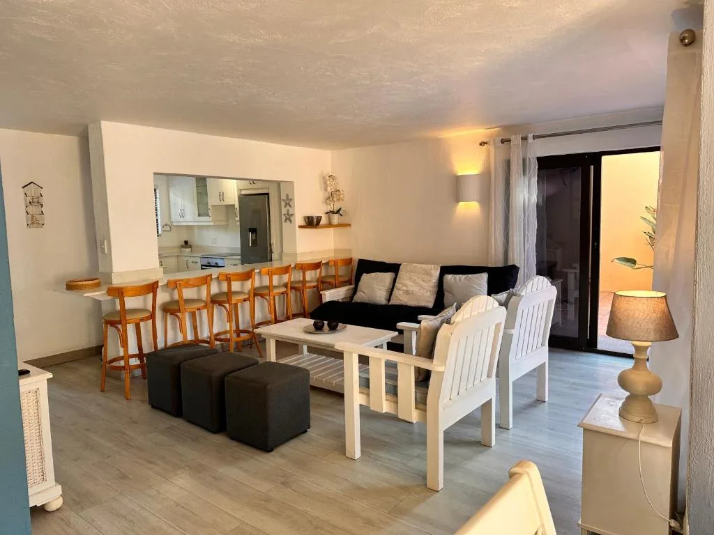 Open-plan lounge with black sofa, white armchairs, and kitchen bar area