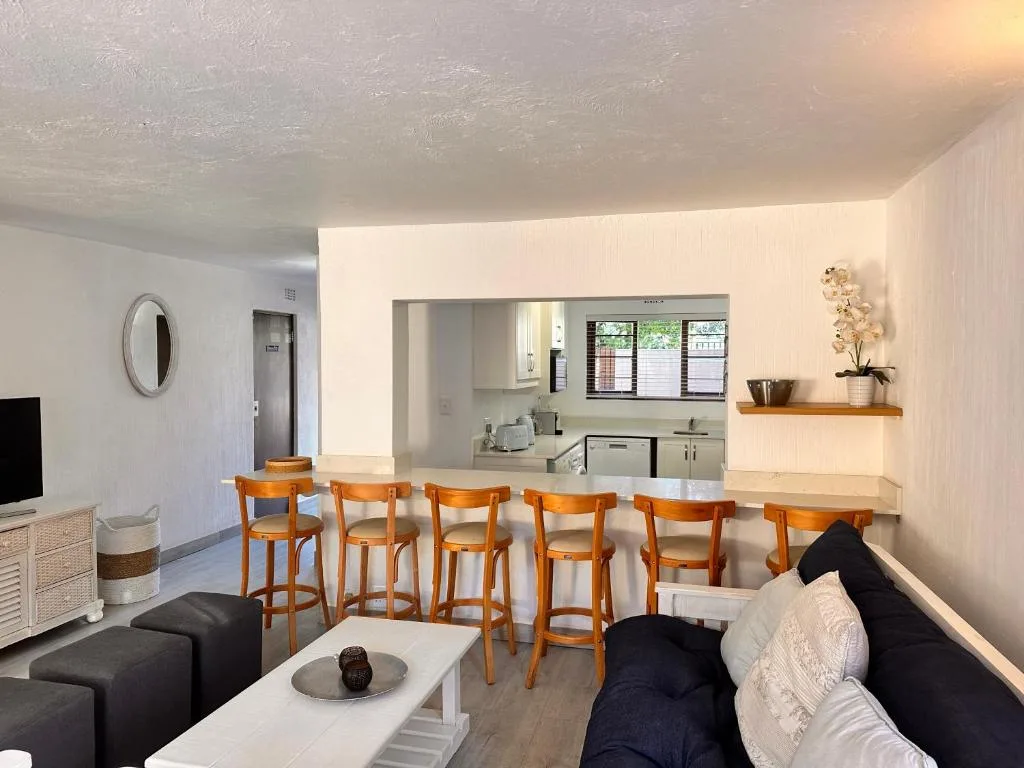 Open-plan lounge with black sofa, wooden bar seating, and kitchen view