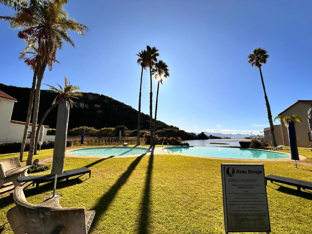 Swimming pool with lounge chairs, palm trees, and lagoon view beyond