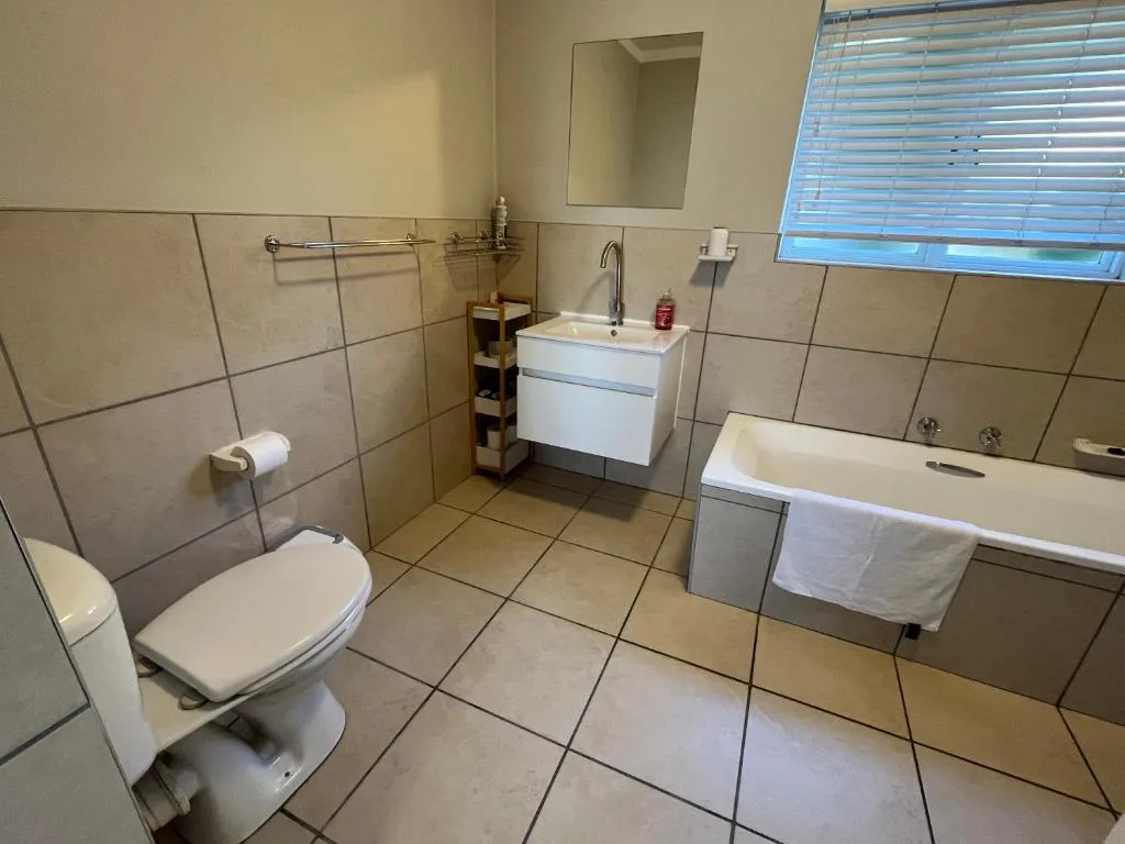 Spacious bathroom with toilet, vanity sink, bathtub, and tiled walls