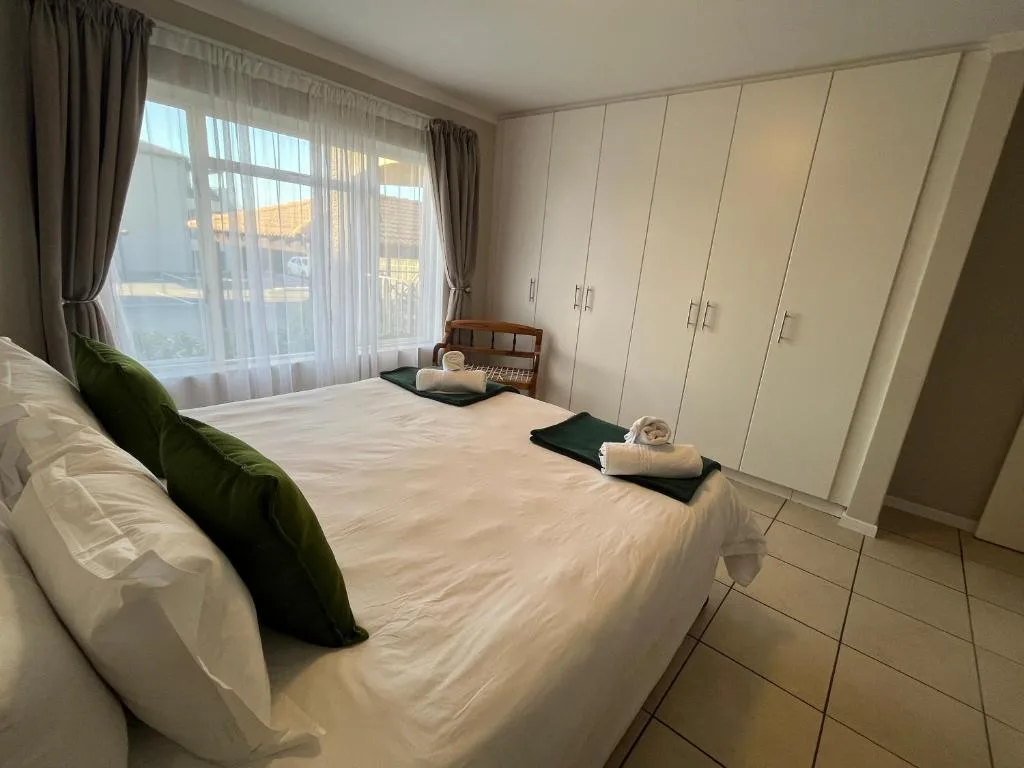 Bright bedroom with double bed, green cushion, large windows, and built-in wardrobes