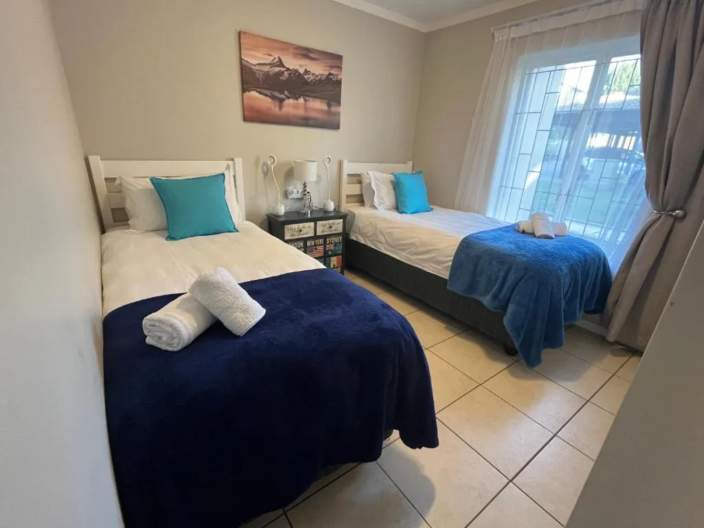 Twin bedroom with dark blue bedding, white pillows, turquoise accents, and patio doors
