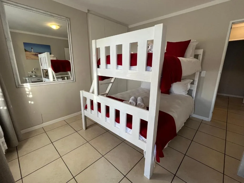 Bright bedroom with white bunk bed and red bedding, mirror, and tiled floor