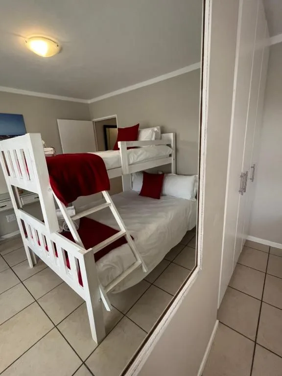 Bright bedroom with white bunk beds, red bedding, and tiled flooring