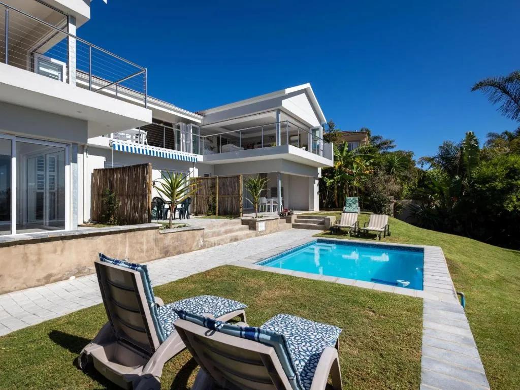 Modern villa exterior with swimming pool, loungers, and manicured garden grounds