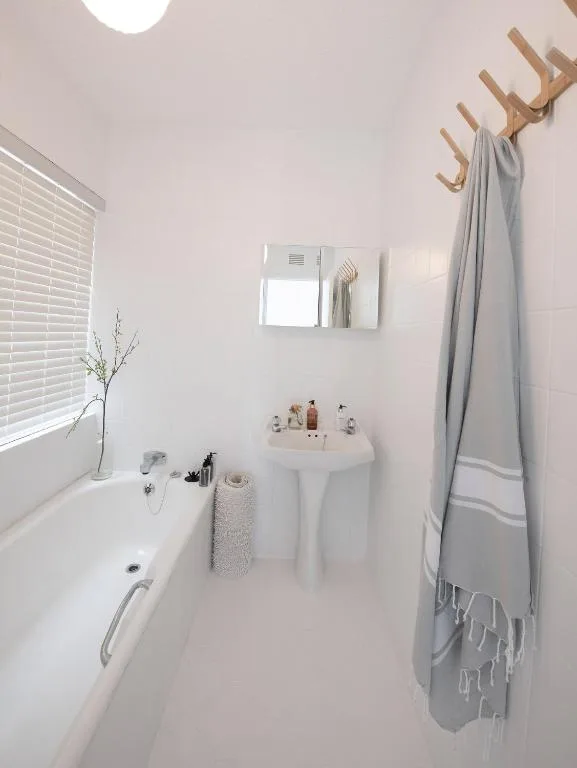 Clean white bathroom with bathtub, pedestal sink, and wooden towel rack