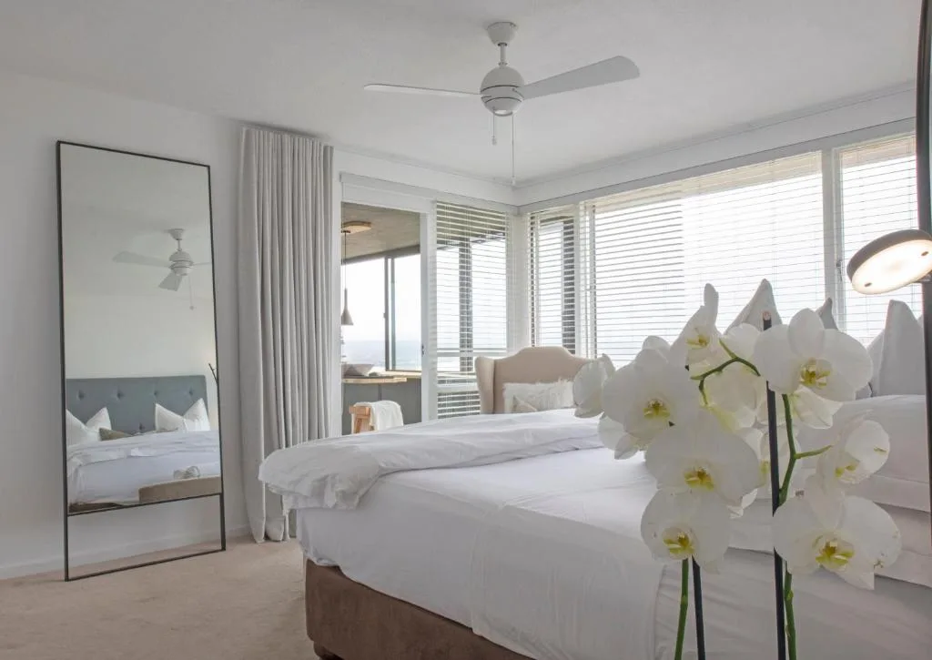 Bright modern bedroom with white orchids, floor-to-ceiling windows, and ocean views