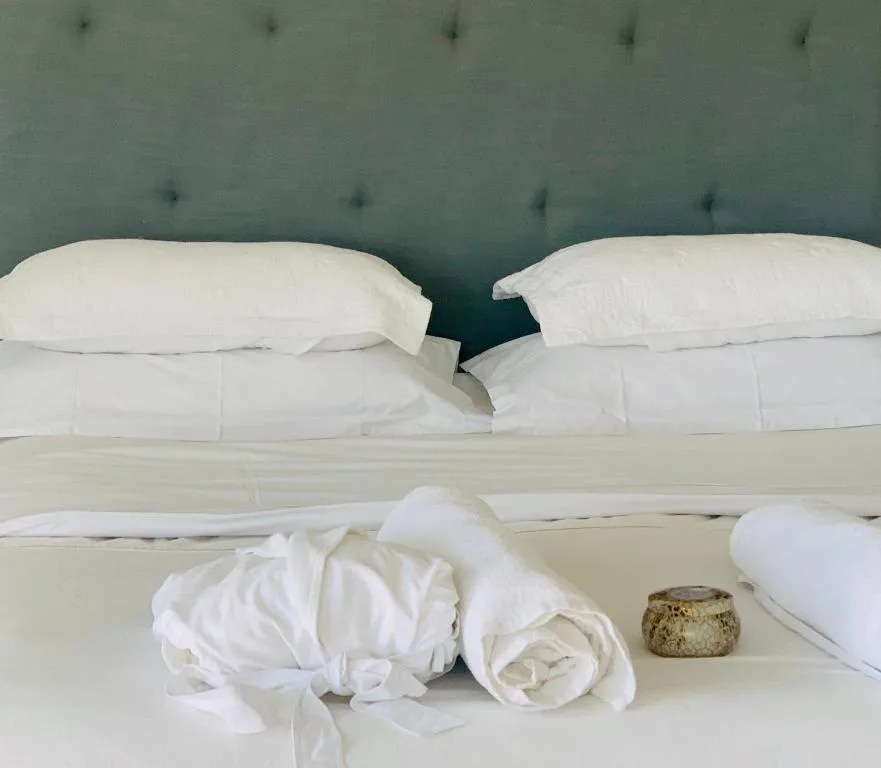 Clean white pillows and bedding with green tufted headboard and amenities