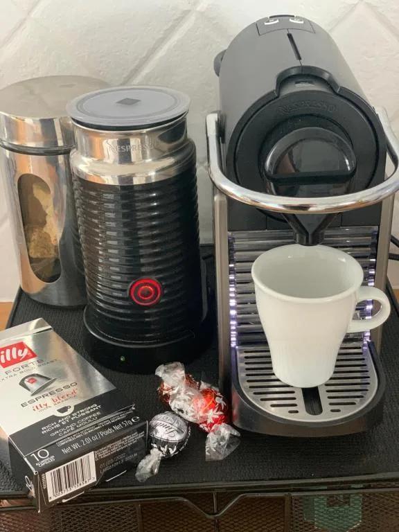 Coffee maker with milk frother, cup, and Illy coffee pods on counter