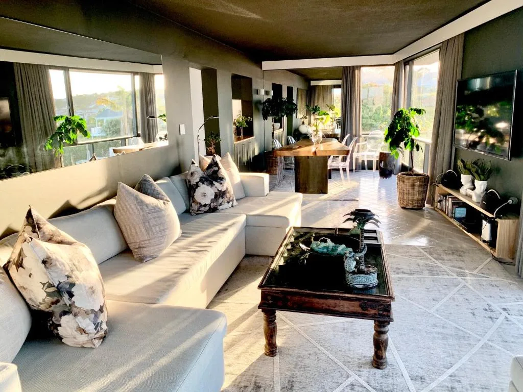 Spacious open-plan lounge with cream sofa, coffee table, plants, and panoramic windows