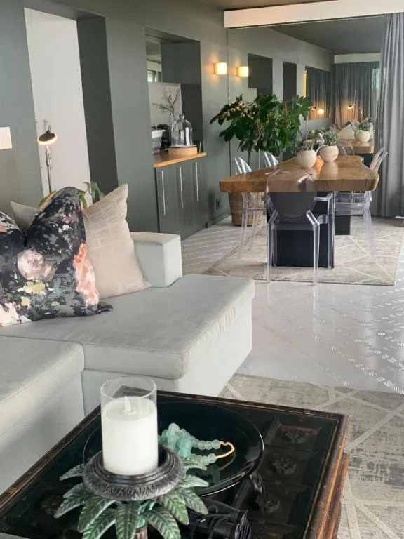 Modern lounge with white sofa, dining table visible beyond, potted plants and decor