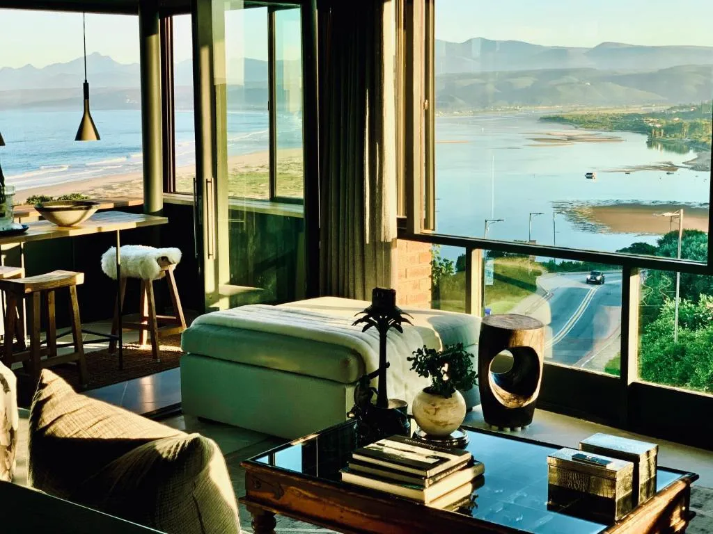 Modern lounge with green ottoman and expansive lagoon views through floor-to-ceiling windows