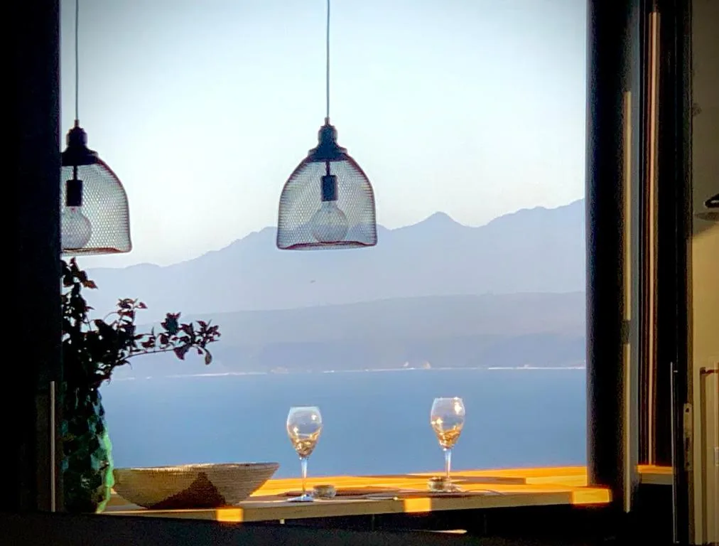 Panoramic coastal vista with mountains, ocean, and wine glasses framed by pendant lights
