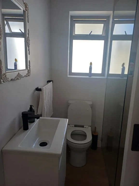 Modern bathroom with white sink, toilet, and shower enclosure with windows