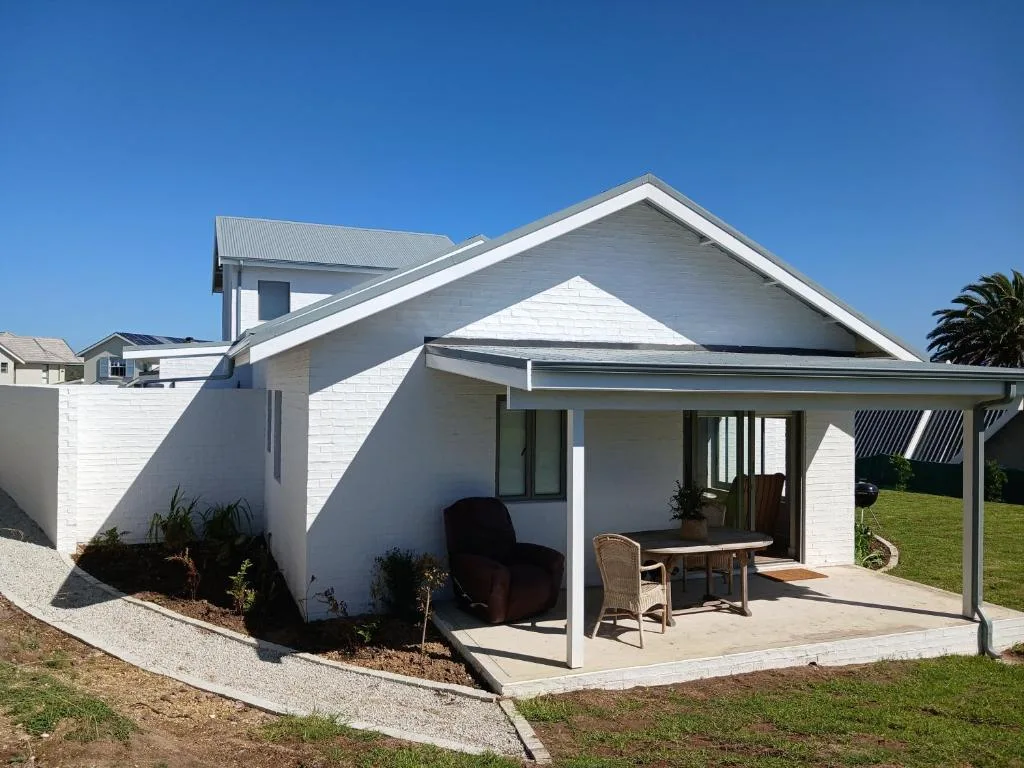 Modern white cottage with covered patio and manicured garden under clear sky