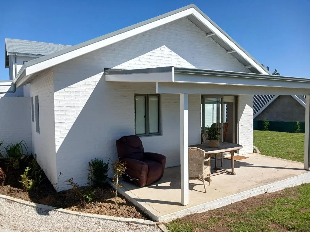 Modern white cottage with covered patio, lounge chair, and manicured lawn