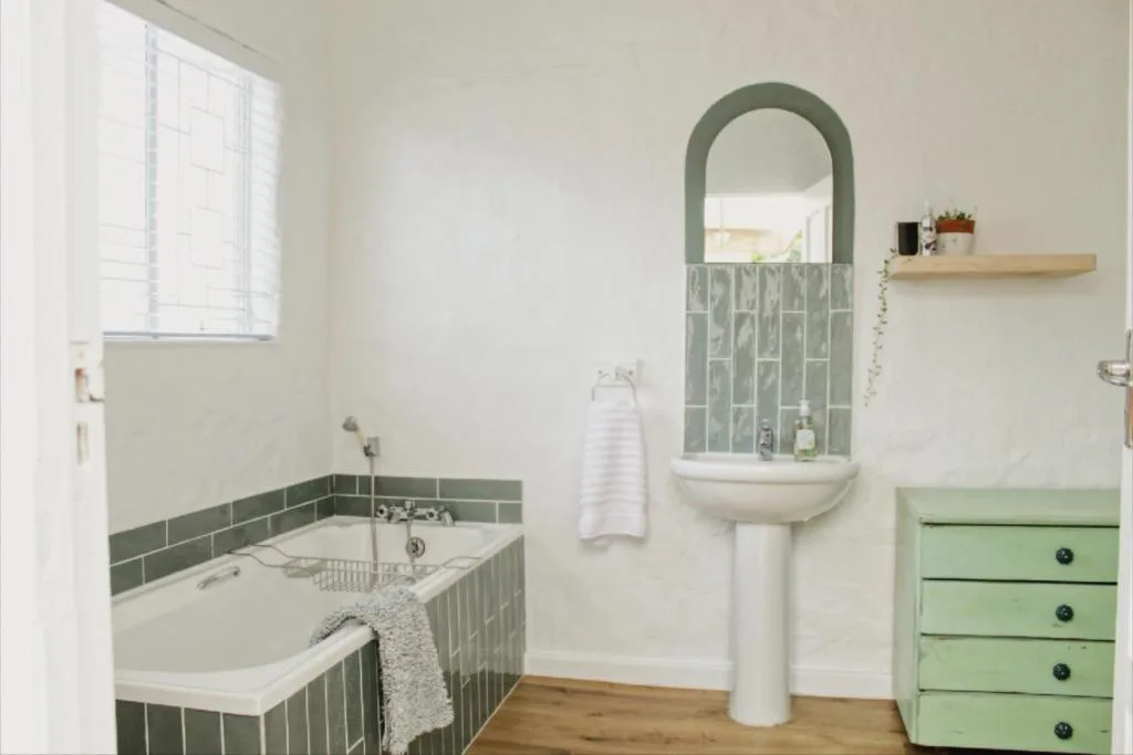 Bright bathroom with soaking tub, pedestal sink, and green tile accents