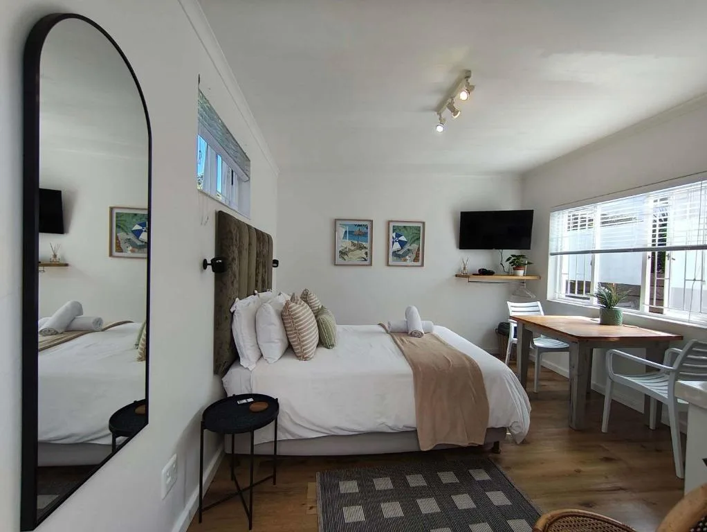 Bright bedroom with queen bed, large mirror, desk workspace, and coastal artwork