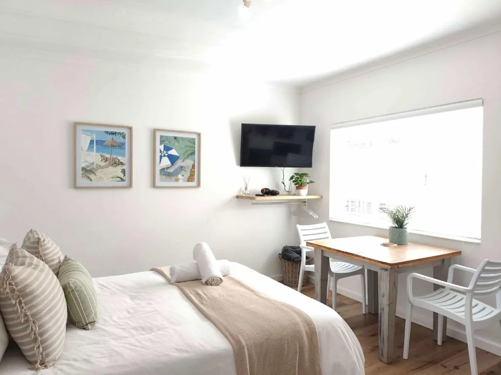 Bright bedroom with queen bed, TV, work desk, and beach-themed wall art