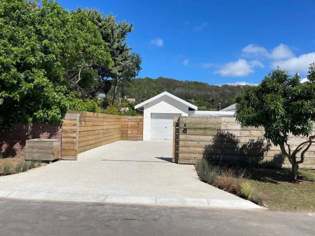 White cottage with wooden gates and gravel driveway surrounded by lush vegetation