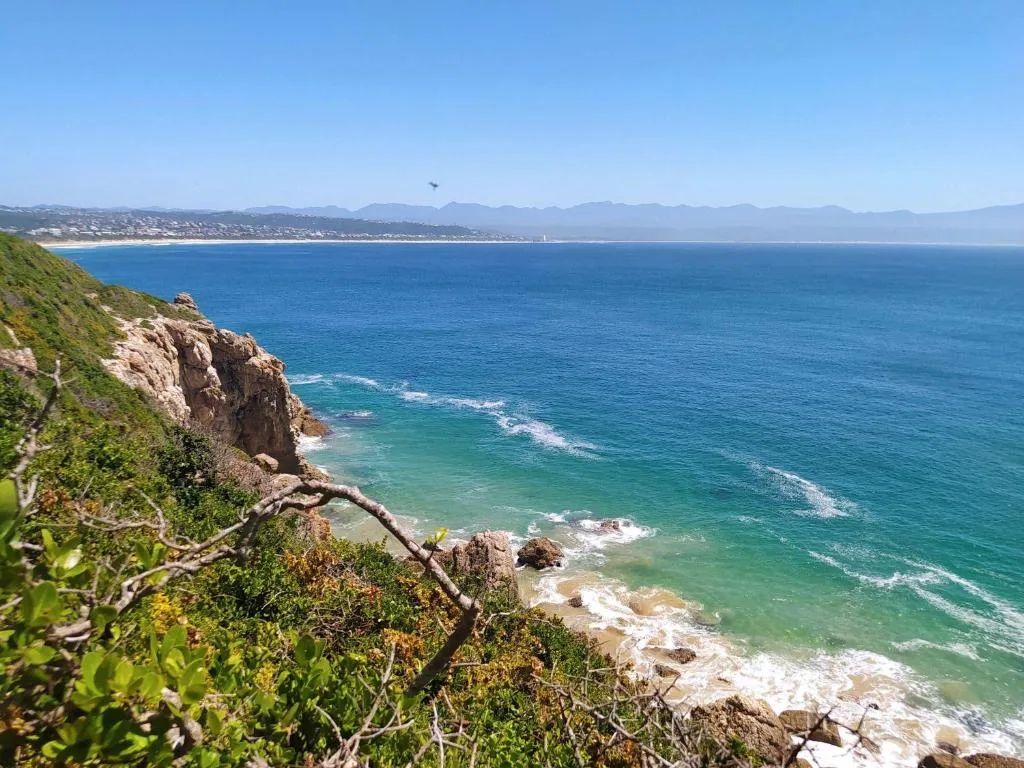 Panoramic coastal view of turquoise ocean, rocky cliffs, and distant coastal town